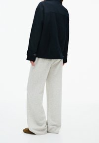 Czarna kurtka o strukturalnym wzorze i zapinanymi mankietami w połączeniu z jasnoszarymi spodniami o szerokich nogawkach, prezentującymi luźny krój i miękki materiał.