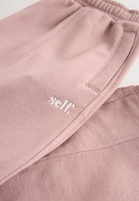 Roze sweatpants gemaakt van een katoenmix-stof, met een elastische tailleband, zijzakken en een geborduurd wit "self." logo.