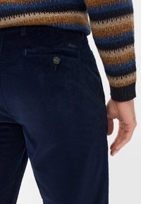 Navyblaue Cordhosen mit vertikalen Rippungen, ausgestattet mit einer Gesäßtasche mit Knopfverschluss und einem kleinen Etikett am Bund.