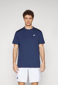 Marineblaue Sport-T-Shirt mit kurzen Ärmeln, Rundhalsausschnitt und weißem Logo. Glatter Stoff, kombiniert mit weißen Shorts für einen kontrastreichen Look.