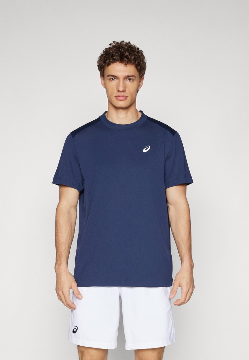 Marineblaue Sport-T-Shirt mit kurzen Ärmeln, Rundhalsausschnitt und weißem Logo. Glatter Stoff, kombiniert mit weißen Shorts für einen kontrastreichen Look.