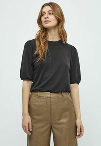 Zwarte top met korte mouwen en opstaande schouders, gecombineerd met hoge beige broek. Zacht stof en ronde halslijn. Minimalistisch ontwerp.