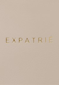 Kermavaalën nahka, jossa on teksturoitu pinta, esittelee kohokuvioitua kultakirjoitusta, joka sanoo "EXPATRIÉ."