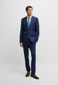 Completo da uomo blu navy con design aderente, chiusura a un bottone e due tasche frontali. Abbinato a una cravatta azzurro chiaro e scarpe marroni.