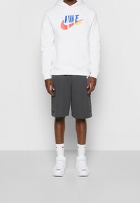 Vit Nike-hoodie med färgglogotyp, grå shorts, vita strumpor och vita sneakers. Outfiten har en enkel design och atletisk stil.