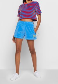 Cropped tričko pruhované v červené a modré barvě spárované s modrými sametovými šortkami s nápisem "TOMMY JEANS" v žluté. Bělé tenisky doplňují outfit.