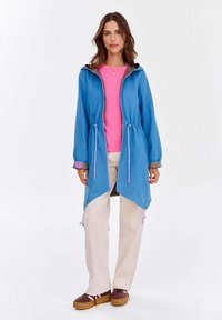 Jasnoniebieska kurtka z kapturem, z troczkami i różowymi akcentami, noszona na różowej bluzce. W połączeniu z beżowymi spodniami i brązowym obuwiem.