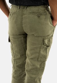 Pantaloni cargo color verde oliva realizzati in tessuto texturizzato, con tasche laterali, vita elastica e due tasche posteriori con chiusura a bottone.