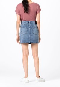 Denim minikjol med fem fickor, ljusblå tvätt, fransad nederkant och hög midja. Matchad med en rosa t-shirt med kort ärm och vita sneakers.