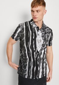 Polo à manches courtes avec un motif abstrait en noir et blanc, un tissu texturé et une patte de boutonnage à trois boutons.