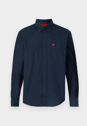 Tengerészkék hosszú ujjú, gombos ing gombos gallérral és mellzsebbel, amelyen egy kis piros logócímke található.