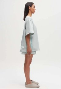 Lichtgrijze oversized t-shirt met korte mouwen, gecombineerd met bijpassende shorts. Bevat een logo en tekst in een subtiel ontwerp. Glad stoffen textuur.