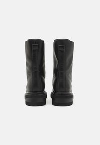 Botas de tobillo de cuero negro con una textura suave, tirador en la parte trasera y una suela de goma gruesa. Diseño minimalista con líneas limpias.