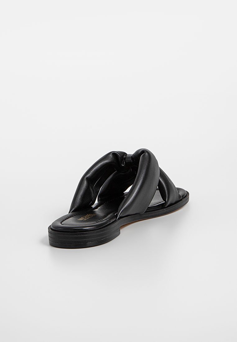 Sandal en cuir noir avec un design noué, semelle plate et texture lisse. Style ouvert avec une esthétique simple et minimaliste.
