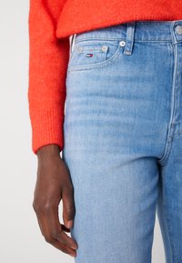 Lys blå jeans i slim fit med fem lommer og subtil bleking. Kombinert med en livlig rød ribbestrikket genser.