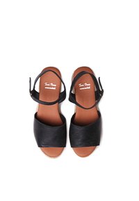 Mustmust musta nahkse sandaalid, millel on lai esirihm, pahkluudega rihm ja beež espadrille-stiilis tald. Textuuriga jalgade alus näitab brändi logo.