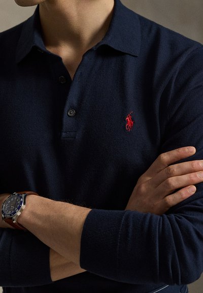 Navy blue polo shirt with a collared neck, short sleeves, and three buttons. Features a red embroidered logo on the left chest and ribbed cuffs.