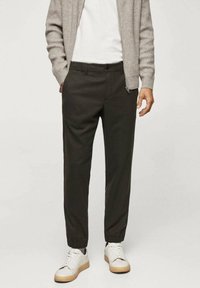 Donkergroene taps toelopende broek met elastische boorden, gecombineerd met een grijs geribbeld vest en witte sneakers met beige zolen. Casual ontwerp.