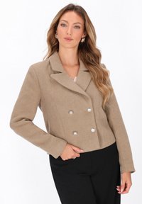 Giacca di lana beige doppiopetto con colletto a revers, bottoni metallici e design cropped. Tessuto liscio, vestibilità su misura.