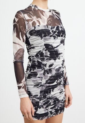 Hun har en ruched, langærmet minikjole på med sorte, hvide og grå abstrakte blomsterprint og gennemsigtige mesh-ærmer.