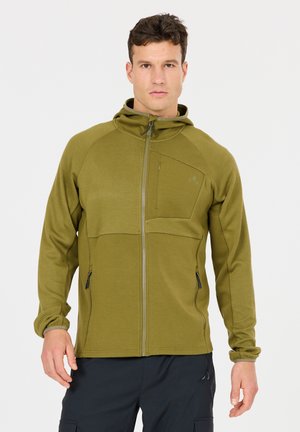 Mann trägt eine olivgrüne Kapuzenjacke mit Reißverschluss, strukturierten Ärmeln und Brusttasche, steht vor einem schlichten weißen Hintergrund.