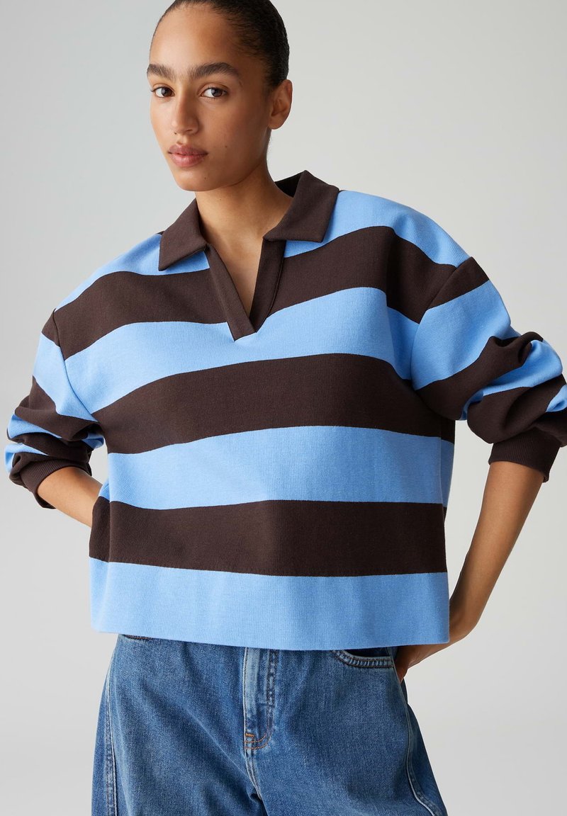 Pullover a righe blu e marroni con scollo a collo e vestibilità rilassata. Realizzato in un tessuto morbido a maglia con maniche arrotolate e orlo corto.