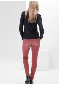 Pantalones de pana rosa, de corte ajustado, con bolsillos traseros, combinados con una blusa oscura de manga larga. Textura suave y diseño hasta el tobillo.