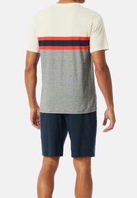 Heren T-shirt met een crème bovenkant, een grijze body en horizontale rode en marineblauwe strepen over de achterkant, gemaakt van zacht katoen.