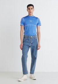 Blue short-sleeve athletic shirt with white accents, paired with light blue denim jeans and white high-top sneakers. Simple design.