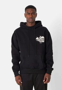 Sudadera negra con bolsillo frontal, que presenta un diseño gráfico en blanco en el lado izquierdo del pecho. Tejido suave y capucha con cordón ajustable.