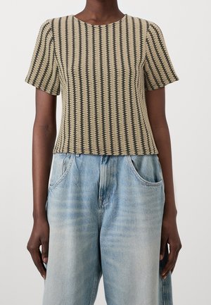 Short-sleeve, beige top with a textured, ribbed design featuring dark brown horizontal stripes, paired with light blue, high-waisted jeans.