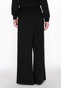 Zwarte wijde broek met een relaxte pasvorm, elastische tailleband en een gladde textuur, met een eenvoudig ontwerp en geen zichtbare patronen of accenten.