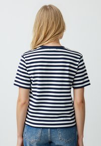 Marineblauw en wit gestreepte t-shirt met korte mouwen, ronde hals en een getailleerd ontwerp. Zachte stof met een lichte rek, gecombineerd met denim jeans.
