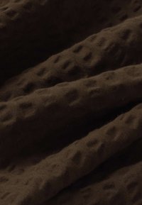 Tissu brun foncé avec un motif texturé en nid d'abeille et des plis doux créant des crêtes ombragées.