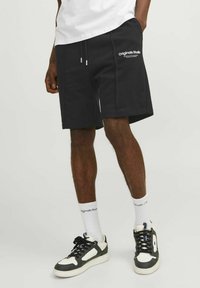 Svarta bomullsshorts med sidofickor, dragsko i midjan, logotypdetalj på låret, kombinerat med svart och vita sneakers och vita strumpor.