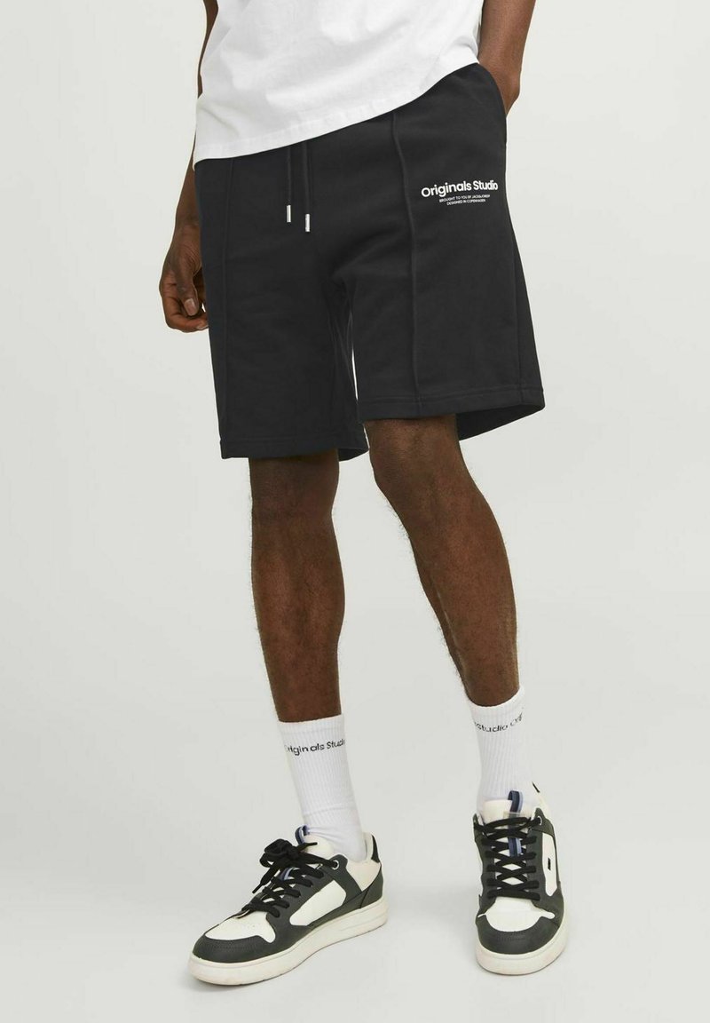 Svarta bomullsshorts med sidofickor, dragsko i midjan, logotypdetalj på låret, kombinerat med svart och vita sneakers och vita strumpor.