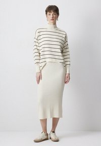 Pletený krémový sveter s čiernymi pruhmi a vysokým golierom, skombinovaný s rebrovanou krémovou midi sukňou a béžovými teniskami.