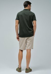 Tmavě zelená polokošile, béžové šortky, strukturovaná tkanina, hnědé semišové boty, jednoduchý design, žádné viditelné vzory ani akcenty.