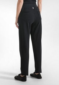 Pantaloni negri cu croială lejeră, talie elastică, două buzunare în spate și deschideri laterale la tiv. Textură netedă a țesăturii.