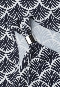 Tissu noir et blanc avec motif abstrait de feuilles et un détail anneau métallique argenté sur l'encolure froncée.