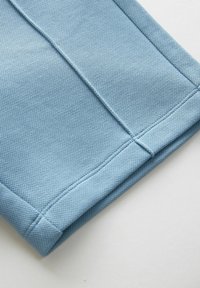 Tissu en coton bleu avec une surface texturée, un bord plié et des coutures renforcées pour plus de durabilité. Lignes épurées sans embellissements supplémentaires.