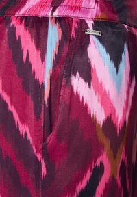 Multicolor stof voor een jurk met een zigzagpatroon in tinten roze, bordeaux en blauw. Metallic merklabel zichtbaar aan de zijkant.