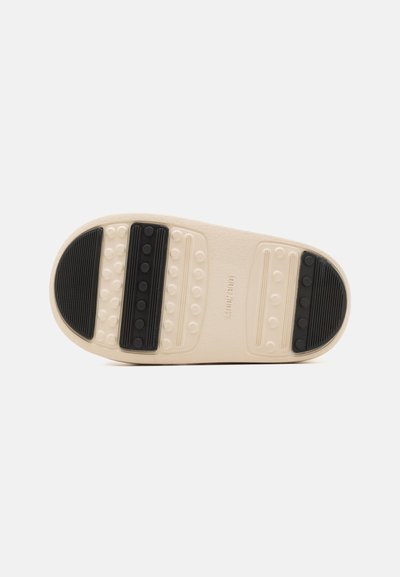Sko sula med en krämig beige bas och texturerade svarta gummidetaljer samt cirkulära greppmönster för bättre grepp.