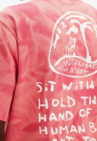 Růžové tričko s tie-dye vzorem obsahující bílé grafické texty a obrázky, včetně palm a unikátních motivů, vyrobené z měkké bavlny.