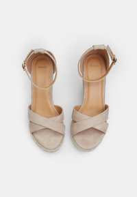 Beige suede sandals with crisscross straps, ankle buckle, and jute-wrapped wedge heels. Smooth inner lining, minimalistic design features.