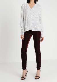 Vit blus med svarta prickar, v-ringning, långa ärmar; ihop med bordeauxfärgade sametsbyxor, figursydda, och svarta remsandaler med klack.