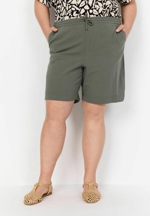 Pantaloni verdi con elastico in vita e coulisse, dotati di tasche laterali e vestibilità slim, abbinati a sandali intrecciati color oro.