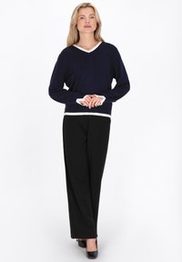 Pulover bleumarin cu decolteu în V și margine albă contrastantă, asortat cu pantaloni negri evazați și pantofi negri, având o textură moale.