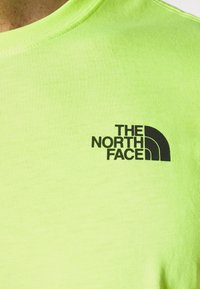 Helles grünes Baumwoll-T-Shirt mit schwarzem "The North Face"-Logo auf der linken Brustseite. Glatte Textur, Rundhalsausschnitt.