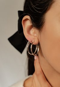 Srebrne kolczyki w kształcie kół, składające się z trzech połączonych pierścieni o różnych rozmiarach. Powierzchnia jest gładka, z lustrzanym wykończeniem.